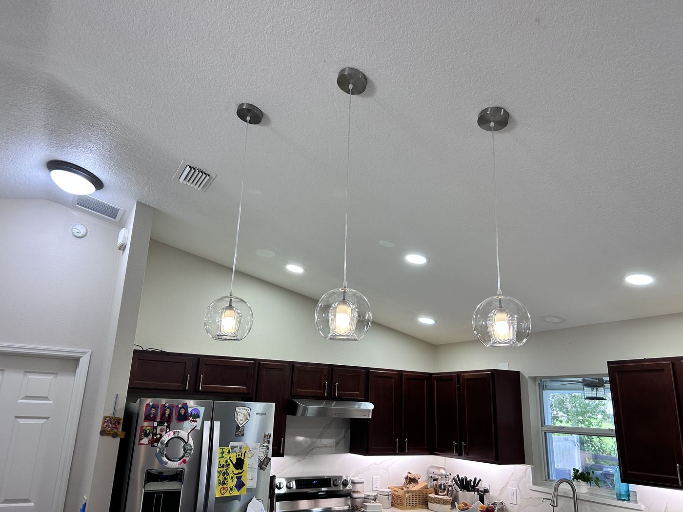 Three glass pendant lights and recessed LED cans installed over a kitchen island